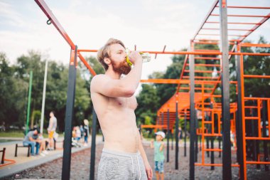 Spor salonundaki antrenmandan sonra spor şişesinden su içen kaslı bir adam. Açık hava eğitiminden sonra susamış bir adam su içiyor. Fitness, spor, yaşam tarzı konsepti. Susuz kalma ve sağlıklı kal..