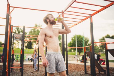 Spor salonundaki antrenmandan sonra spor şişesinden su içen kaslı bir adam. Açık hava eğitiminden sonra susamış bir adam su içiyor. Fitness, spor, yaşam tarzı konsepti. Susuz kalma ve sağlıklı kal..