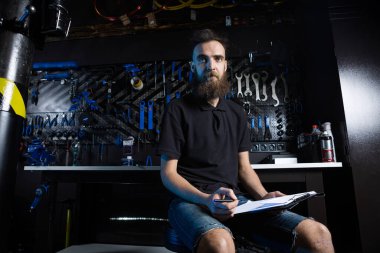 Bisiklet Atölyesi Teknisyeni İdari İşler yapıyor. Kontrol listesi defterine bisiklet tamircisi yazıyormuş. İş yerinde bisiklet tamircisi. Bisiklet dükkanında beyaz işçi panoya yazı yazıyor..