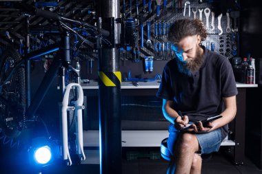 Bisiklet tamircisi atölyedeki panoya not alıyor. temalı küçük işletme satışı, onarım ve servis bisikletleri. Bisiklet dükkanında idari evrak işleriyle uğraşan teknisyen. İşi yönet.