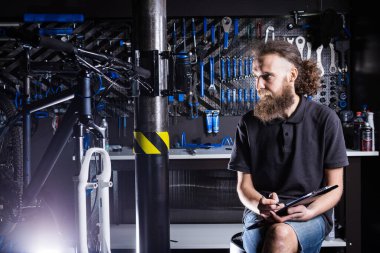 Bisiklet Atölyesi Teknisyeni İdari İşler yapıyor. Kontrol listesi defterine bisiklet tamircisi yazıyormuş. İş yerinde bisiklet tamircisi. Bisiklet dükkanında beyaz işçi panoya yazı yazıyor..