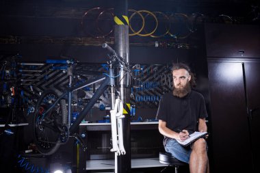 Bisiklet tamircisi atölyedeki panoya not alıyor. temalı küçük işletme satışı, onarım ve servis bisikletleri. Bisiklet dükkanında idari evrak işleriyle uğraşan teknisyen. İşi yönet.