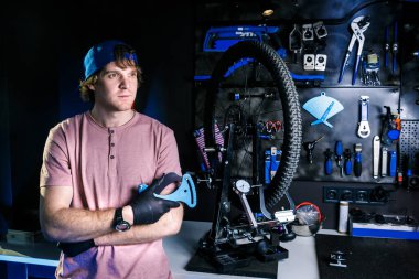 Küçük bir bisiklet tamirhanesi teması. Atölye sahibi şık bir adam arka planda aletle tekerleği tamir etmek için makinenin yanında duruyor. Telleri germek için gerekli aletleri elinde tutuyor.