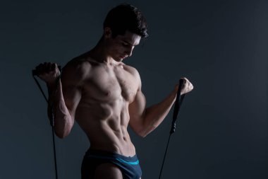 Kas Fitness genç erkek antika mükemmel kaslar altı paketleri ABS ve çıplak göğüs. Stüdyodan karanlık bir arka plana karşı streç elastik ile vücut geliştirmeci Model trenler. Egzersiz eğitim spor salonu.