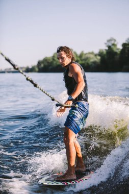 Aktif uyanış uzmanı nehir dalgalarının aşağısına atlıyor. Dalgada sörfçü. Erkek sporcu Wakesurf eğitimi alıyor. Açık havada aktif su sporları. Bir adam sörf yaparken dalga yakalar..
