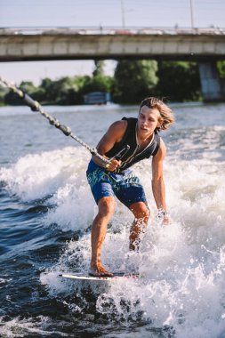 Bir adam sörf tahtasının üzerinde sörf yapıyor. Teknenin üstünde bir motorlu tekne çiziyor. Weixerfer sörf, eğlence, eğlence ve su sporlarıyla meşgul. Sporcu sörf tahtasındaki dalgalarda kayar.