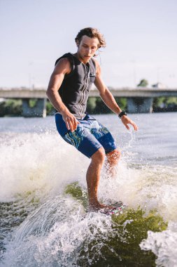 Bir adam sörf tahtasının üzerinde sörf yapıyor. Teknenin üstünde bir motorlu tekne çiziyor. Weixerfer sörf, eğlence, eğlence ve su sporlarıyla meşgul. Sporcu sörf tahtasındaki dalgalarda kayar.