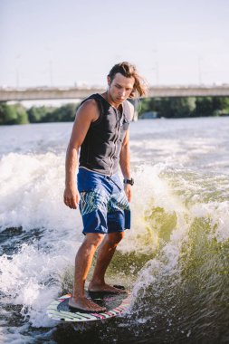 Bir adam sörf tahtasının üzerinde sörf yapıyor. Teknenin üstünde bir motorlu tekne çiziyor. Weixerfer sörf, eğlence, eğlence ve su sporlarıyla meşgul. Sporcu sörf tahtasındaki dalgalarda kayar.