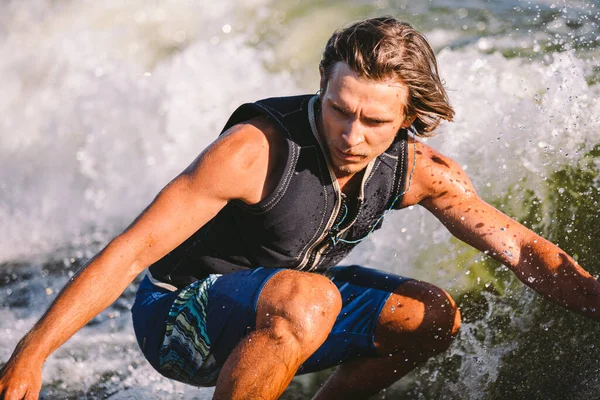 Active wakesurfer jumping on wake board down the river waves. Surfer on wave. Male athlete training on wakesurf training. Active water sports in open air on board. A man catches a wave on surf.