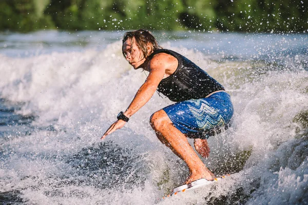 A man is surfing on a surfboard drawn by a motor boat above the wave of the boat. Weixerfer is engaged in surfing, entertainment, leisure, water sports. Athlete glides on the waves on the board.