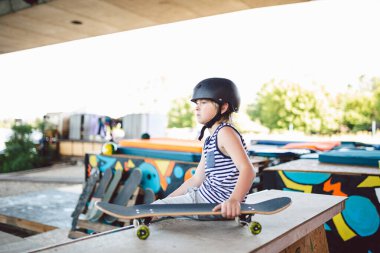 Modayı takip eden kaykaycı çocuk kaykay parkında keyfine bakıyor, yarım rampada oturuyor. Paten kaydıktan sonra dinleniyor. Çocuk spor sahasında kaykayla rahatlıyor. Çocuk rampada oturuyor, arkadaşlarını bekliyor.