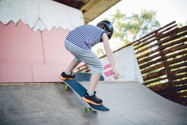 Kasklı beyaz çocuk dışarıda kaykay yapmak için oyun parkında kaykay yapıyor. Bir çocuk kaykaycı kaykay parkında yarım boru rampasına biner. Ekstrem spor ve çocuklar.