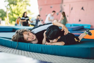 Trambolinde uzanan mutlu çocuklar. Kardeşler spor salonunun dışındaki trambolinde spor minderinde yatarken eğleniyorlar. Çocuklar eğitimden sonra birbirlerini şımartır, güler ve kucaklarlar..