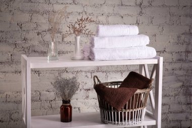 Üç beyaz havlu yığını ve temiz kahverengi havlular ve tuğla duvarın yanında tuvalet dekoru olan sepetler. Havluları ve dekoratif vazoları olan raflar. Raflar temiz havlularla dolu..