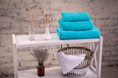 Üç renkli turkuaz havlu ve temiz beyaz havlularla dolu sepetler ve tuğla duvarın yanında tuvalet dekoru. Havluları ve dekoratif vazoları olan raflar. Raflar temiz havlularla dolu..