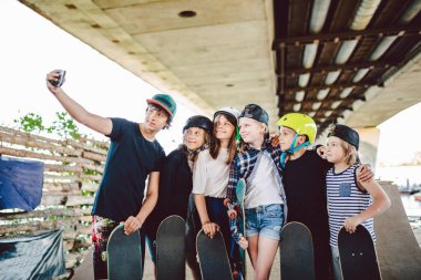 Bir grup kaykaycı, kaykay parkında telefonda selfie çekiyor. Kaykaylı büyük bir grup çocuk kaykay parkındaki rampada hafıza fotoğrafı çekiyor. Grup çocukları akıllı telefondan ortak fotoğraf çekiyorlar..