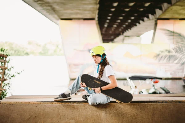 Schoolgirl after lessons at skateboarding practice in outdoor skate park. Stylish and beautiful caucasian girl with skateboard on a half pipe ramp in a skatepark. Teenager skater girl with skate deck.