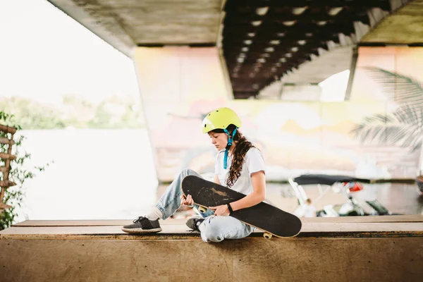 屋外スケートパークで自信を持って クールな若い女性のスケートボーダー パイプランプの半分にスケートボードを持つ都市の女の子 生活様式 ティーンモデルスケボーポーズでヘルメットとスタイリッシュな服 — ストック写真