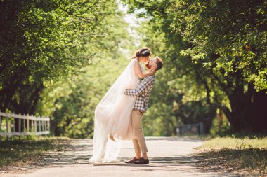 Mutlu damat yaz parkında gelin yetiştiriyor. Adam kadını kollarına alıp kucakladı. Parkta yeni evli bir çift. Yeni evlendim. Parkta yürü ve sarıl. Yeni evliler eğleniyor. Kırsal düğün.