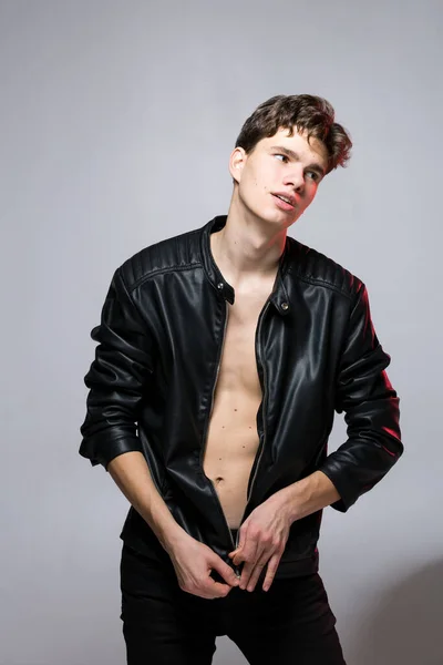 Handsome caucasian guy model with naked tors, lack leather jacket posing in studio on red background. Sexy young man in black stylish clothes on naked body. Emotional posing, lifestyle people concept.