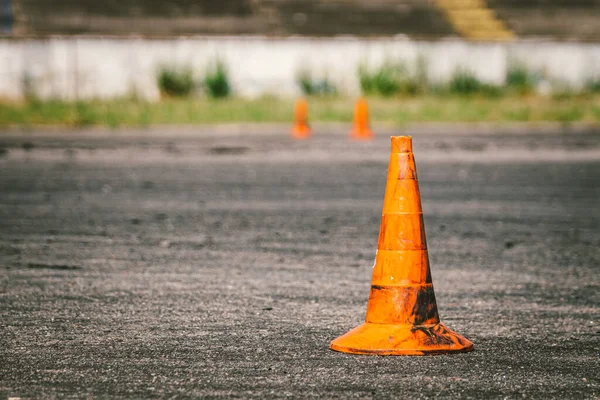 Close-up of an old dirty orange traffic cone at the site for driving training or auto school. Plastic red markings at the autodrome, extreme driving stadium. Driving school concept.