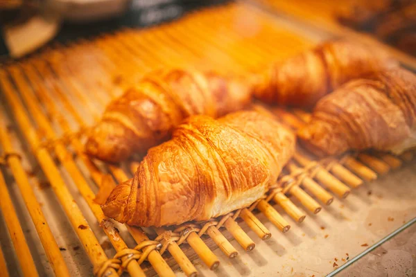 Pastanedeki vitrinde kruvasan var. Dükkan vitrinindeki kafede iştah açıcı altın kruvasanları kapatıyoruz. Pasta şefi tarafından yapılan lezzetli ve tereyağlı kruvasan çeşitleri. Doğal ışık.