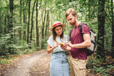Yürüyüşçüler yön bulmak için mobil GPS kullanıyorlar. Sırt çantası gezisi sırasında ormanda akıllı telefonu kontrol eden mutlu çift. GPS haritası, navigatör konum belirleme uygulaması kullanan neşeli genç bir çift. Aşk ve seyahat kavramı.