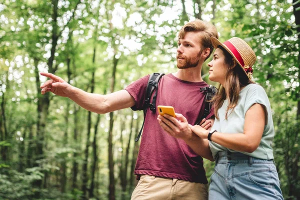 Couple hiking and using maps app on cell phone. Two people hikers looking at mobile phone trying find route. Hike in forest, looking smartphone, search tourist attraction, adventure travel concept.