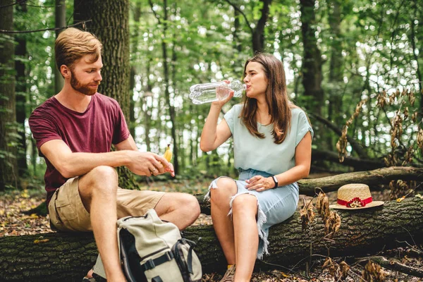 ログと飲料水の上に座ってリラックスカップル 家族は自然の中でロマンチックな週末を楽しんでいます 自然を背景にした快適な散歩やロマンチックなデート 森の中のピクニックハイキング — ストック写真