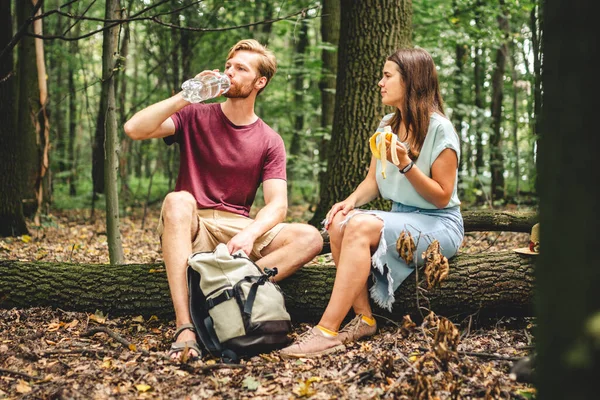 若い夫婦は倒木の道を歩いて森の中で休むために座って 人々は水を飲み バナナの実を食べる 観光客は軽食や補充の水のバランスを破る 自然界の食べ物や飲み物 — ストック写真