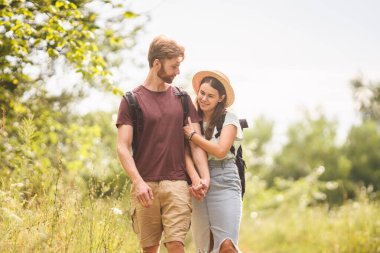 Kafkasyalı hippi çift kırsal yolda yürüyor. Sırt çantasıyla doğa parkında yürürken sevgili kızının elini tutan sakallı bir adam. Seyahat, yürüyüş, turizm ve insan konsepti.