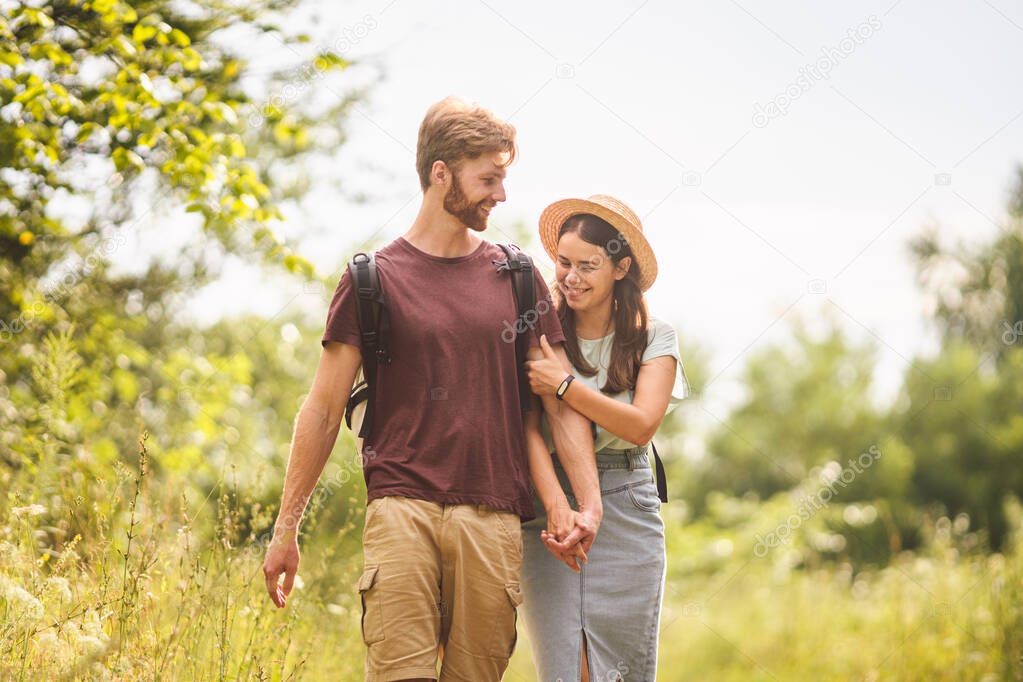 Couple Hiking Along Woodland Path. Happy loving man and woman on holiday walking together. Active lifestyle concept. Young people walking with backpacks on country road outdoors.