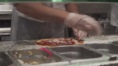 Fast food restoranındaki şefin elleri pizza görüntüsüne malzeme koydu. Pizza konsepti. Yiyecek üretimi ve teslimatı. Lezzetli, malzeme. 4K çözünürlükte vuruldu. İtalyan yemeği.