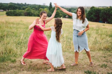 Üç yetişkin Kafkas kız kardeş sahada oynuyorlar ve eğleniyorlar. Üç genç bayandan oluşan bir aile gülüyor ve yaz mevsimini doğada geçiriyor. Mutlu çocuk, anne ve kız kardeş koşun ve dışarıda oynayın.