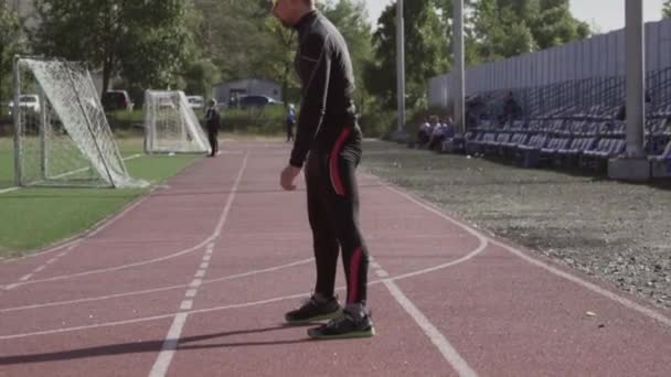 2 de marzo de 2019. Ucrania, Kiev. Tema deporte y salud. Hombre caucásico joven hace ejercicio de calentamiento estiramiento de los músculos antes de entrenar en correr en un estadio de la ciudad cinta de correr — Vídeos de Stock