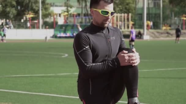 2. března2019. Ukrajina, Kyjev. Téma sport a zdraví. Mladý kavkazský muž dělá cvičení zahřát protahování oteplování svalů před tréninkem v běhu na městském stadionu běžecký pás — Stock video