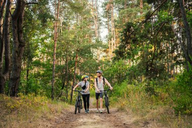 Park Ormanı 'nda bisiklete binen muhteşem bir çift. Bisikletle romantik bir gezi. Aktif hafta sonu. Spor çifti. Erkek ve kadın bisikletçiler. Çevre dostu ulaşım. Yoldaki dağ bisikletleriyle dolu..