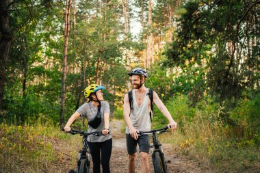 Park Ormanı 'nda bisiklete binen muhteşem bir çift. Bisikletle romantik bir gezi. Aktif hafta sonu. Spor çifti. Erkek ve kadın bisikletçiler. Çevre dostu ulaşım. Yoldaki dağ bisikletleriyle dolu..