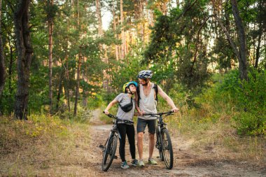 Park Ormanı 'nda bisiklete binen muhteşem bir çift. Bisikletle romantik bir gezi. Aktif hafta sonu. Spor çifti. Erkek ve kadın bisikletçiler. Çevre dostu ulaşım. Yoldaki dağ bisikletleriyle dolu..