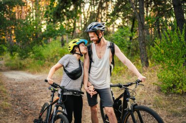 Park Ormanı 'nda bisiklete binen muhteşem bir çift. Bisikletle romantik bir gezi. Aktif hafta sonu. Spor çifti. Erkek ve kadın bisikletçiler. Çevre dostu ulaşım. Yoldaki dağ bisikletleriyle dolu..
