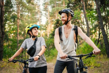 Genç beyaz bisikletçiler parktaki orman yolunda dağ bisikletlerini yürütür ve iterler. Aktif spor hafta sonu. Kırsalda bisikleti olan güzel insanlar..