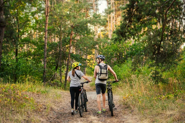 Gorgeous couple riding on bikes in park forest. Romantic trip by bicycles. Active weekend. Sport couple. Man and woman cyclists. Eco friendly transportation. ouple with mountain bikes on the path.