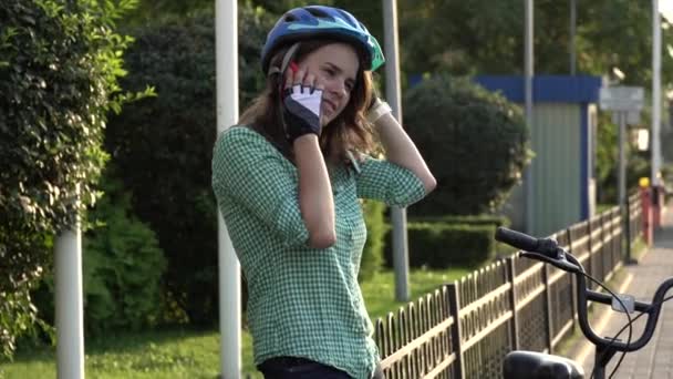 Retrato de una chica alegre sosteniendo el teléfono móvil. Feliz estudiante sonriente utilizando la aplicación para compartir bicicletas en el teléfono inteligente al aire libre. Estilo de vida de la ciudad chica hipster con estilo con la bicicleta usando aplicación de teléfono inteligente en la calle — Vídeo de stock