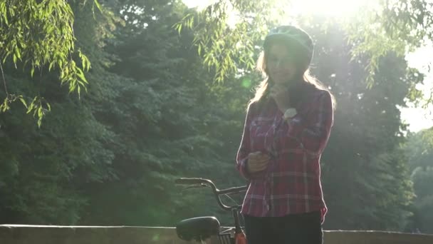 자전거는 자전거를 이용 한 교통 수단이다. 파란색 헬멧을 쓰고 긴 머리를 한 젊은 백인 여성이시 공원에서 바구니를 든 오렌지 색 렌터카 옆에 서 있다. — 비디오