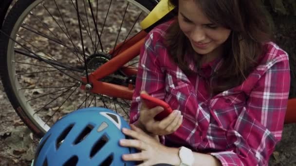 Ποδηλάτης χρησιμοποιούν κινητό τηλέφωνο, ενώ ιππασία ποδήλατο. Νεαρή γυναίκα με ποδήλατο χρησιμοποιώντας smartphone στο πάρκο. Νεαρή γυναίκα σε κύκλο στο ξύλο ελέγχοντας το κινητό τηλέφωνο. Ένα κορίτσι που κάνει διάλειμμα στο δάσος. Αθλητισμός και Τεχνολογία — Αρχείο Βίντεο