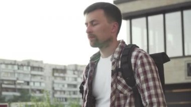 Sırt çantalı beyaz bir adam, elinde katlanmış bir elektrikli scooterla bir ofis binasının merdivenlerinden yukarı çıkıyor. E-scooter 'ı iş yerinden katlanmış olarak taşıyan adam