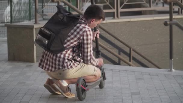 Чоловік тримає складений E-Scooter в руці на сходах біля будівлі. Переїзд екологічним міським транспортом, сучасна концепція міста. Екологічний технологічний спосіб життя. Людина носить електричний скутер у складеному положенні — стокове відео