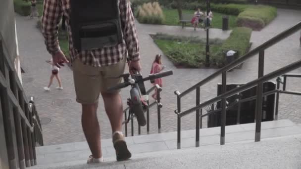 Man wandelen met gevouwen elektrische scooter de trap op in de stad in de buurt van modern gebouw. Ecologische technologische levensstijl. E-mobiliteit. Persoon met elektrische scooter gevouwen positie. Eco-stedelijk vervoer — Stockvideo