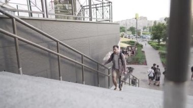 Modern binanın yakınlarında katlanmış elektrikli scooterla yürüyen bir adam. Ekolojik teknolojik yaşam tarzı. E-Hareket kabiliyeti. Elektrikli Scooter 'ı taşıyan kişi katlanmış pozisyonda. Çevre taşımacılığı