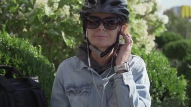 Orta yaşlı insanlar aktif yaşam tarzı konsepti. Yetişkin bir kadın gelişir, zamana ayak uydurur ve şehir parkında aletler kullanır. Yaşlı bir kadın kulaklıkla müzik dinliyor, elektrikli scooter kullanıyor.